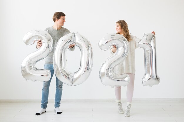 Feiertags-, Fest- und Partykonzept - Glückliches Liebespaar hält silberne 2021 Luftballons auf Weiß