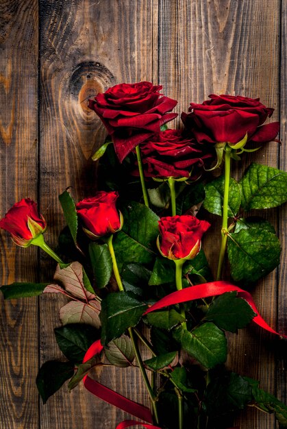 Feiertagshintergrund, Valentinstag. Strauß roter Rosen, Krawatte mit roter Schleife. Auf einem Holztisch