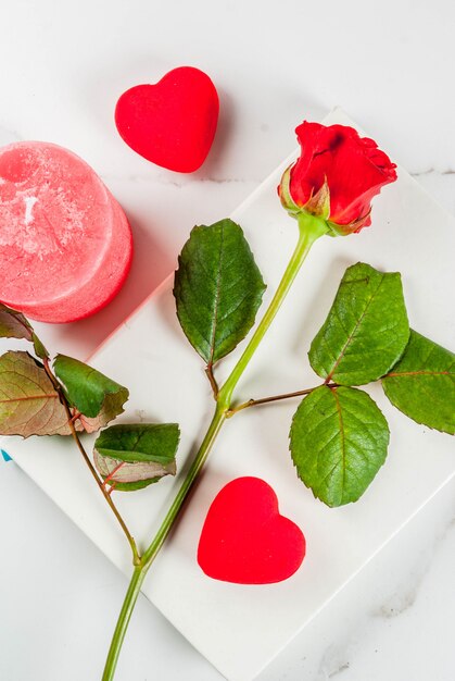 Feiertagshintergrund, Valentinstag. Strauß roter Rosen, Krawatte mit roter Schleife, mit leerem Notizblock, umwickelter Geschenkbox und roter Kerze. Auf einer weißen Marmortischplatteansicht