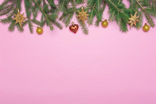 Feiertagsrahmen von Weihnachtsdekorationen auf rosa Hintergrund mit Tannenzweig