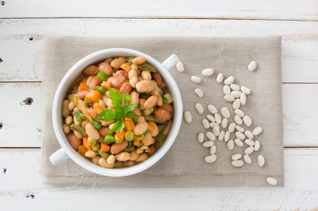 Foto feijão branco com legumes na vista superior de mesa de madeira branca