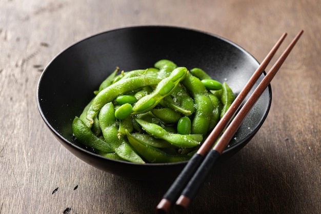 Feijão de edamame de soja em uma tigela de cerâmica preta em foco seletivo de fundo de madeira