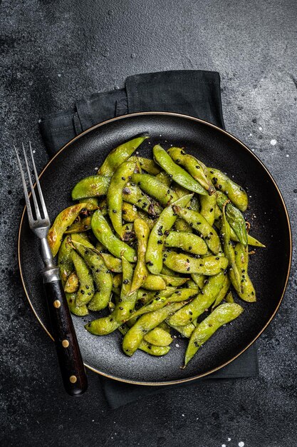 Feijão de soja Edamame verde salteado com sal marinho e sementes de gergelim em um prato Fundo preto Vista superior