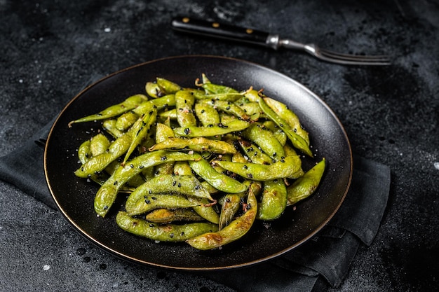 Feijão de soja Edamame verde salteado com sal marinho e sementes de gergelim em um prato Fundo preto Vista superior