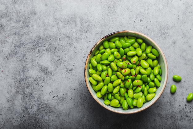 Feijão edamame verde maduro fresco sem vagens em uma tigela sobre fundo de pedra cinza com espaço para texto. Vista superior, close-up. Lanche asiático leve e saudável, boa fonte de proteína para dieta e nutrição