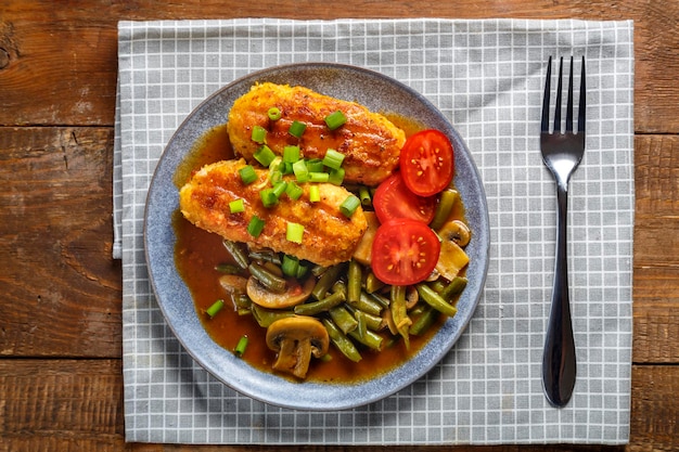 Foto feijão verde com champignon e costeletas polvilhadas com cebolinha em um prato sobre uma mesa de madeira em um guardanapo cinza