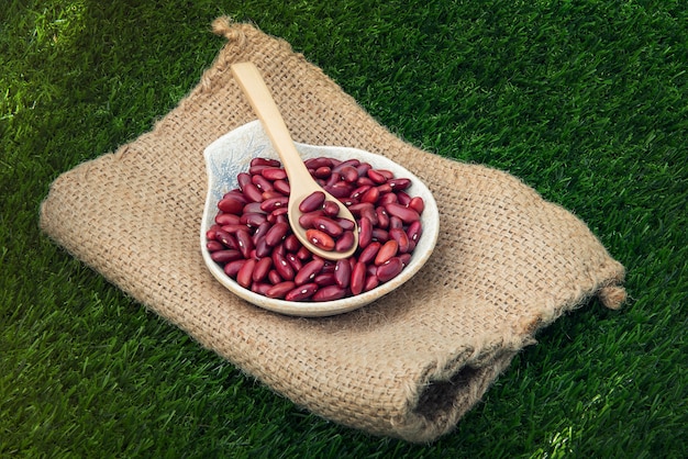 Feijão vermelho de cereais em uma tigela de madeira e colher na parede de grama