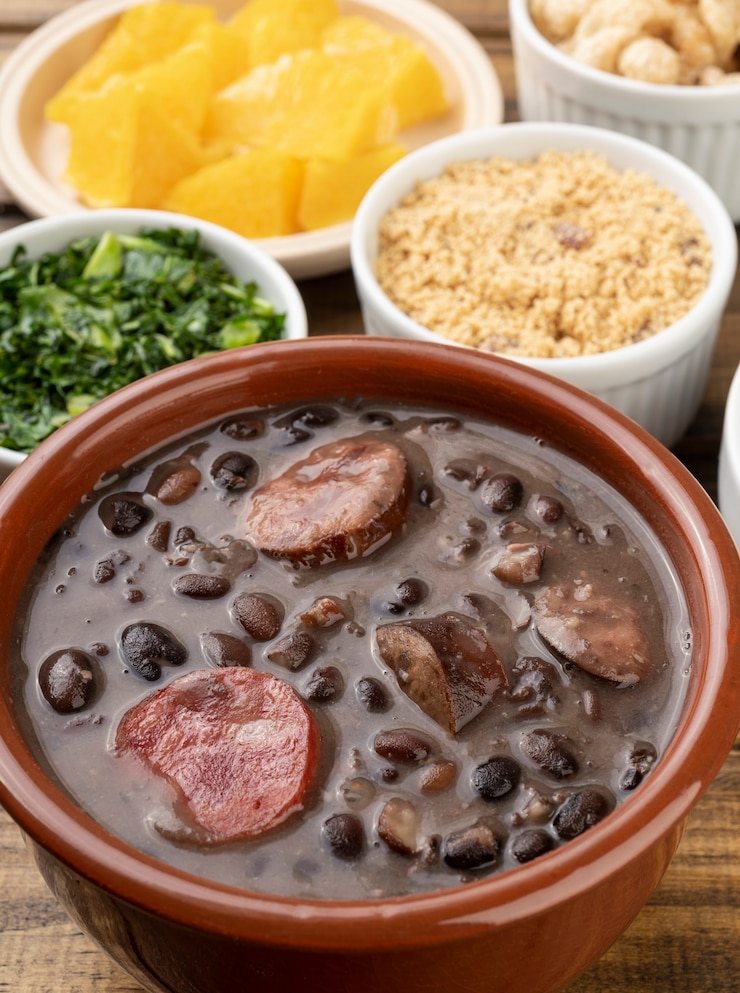 Foto feijoada tradicional com laranja, couve e farinha de mandioca.