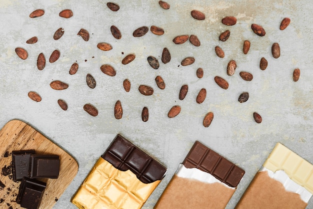 Foto feijões de cacau dispersados ​​e diferentes barras de chocolate no fundo de concreto