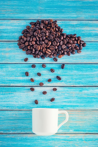 Feijões de café na forma da nuvem chuvosa com o copo no fundo azul. Conceito de tempo