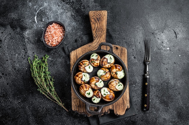 Feinkost - Bourgogne Escargot Schnecken mit Knoblauchbutter in einer Pfanne. Schwarzer Hintergrund. Ansicht von oben.