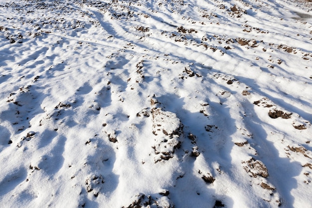 Feld, in dem es Spuren und Spuren von Autos gibt. In der Winterzeit des Jahres ist der Boden nach einem Schneefall mit weißem Schnee bedeckt. Nahaufnahme genommen