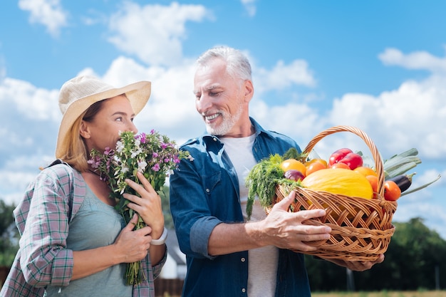 Feldblumen. Blonde Frau mit beigem Hut, die sich überrascht und erfreut fühlt, nachdem sie Feldblumen von ihrem Mann erhalten hat