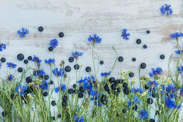 Felder Blumen und Beeren über hellblauem Holztisch