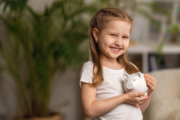 Felices ahorros. Una niña linda con una alcancía en casa