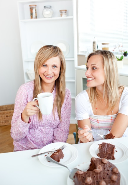 Felices amigas comiendo un pastel de chocolate y bebiendo en el