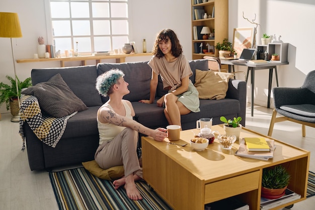 Felices amigas jóvenes en ropa informal mirándose durante el desayuno