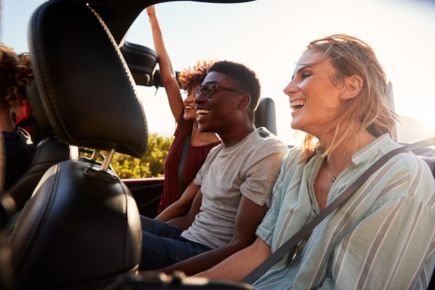 Felices amigos adultos jóvenes en un viaje de vacaciones por carretera viajando en la parte trasera de un auto abierto