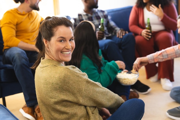 Foto felices amigos y amigas diversas hablando comiendo palomitas de maíz y bebiendo cerveza en casa