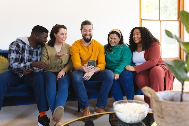 Foto felices amigos y amigas diversos relajándose en casa juntos hablando y mirando el teléfono inteligente