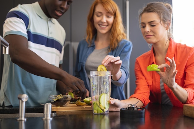 Felices amigos diversos haciendo bebidas saludables juntos en la cocina