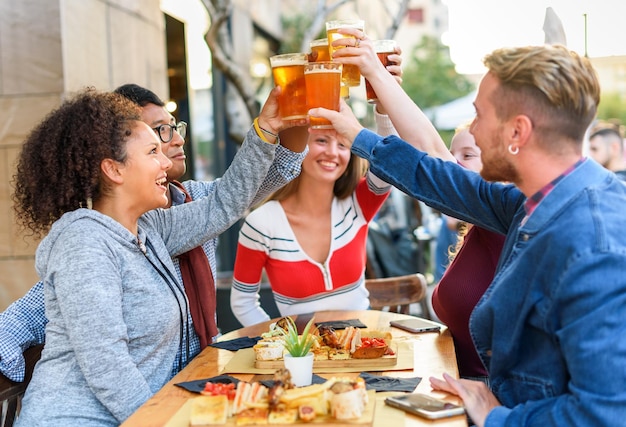 Felices amigos diversos haciendo sonar vasos de cerveza