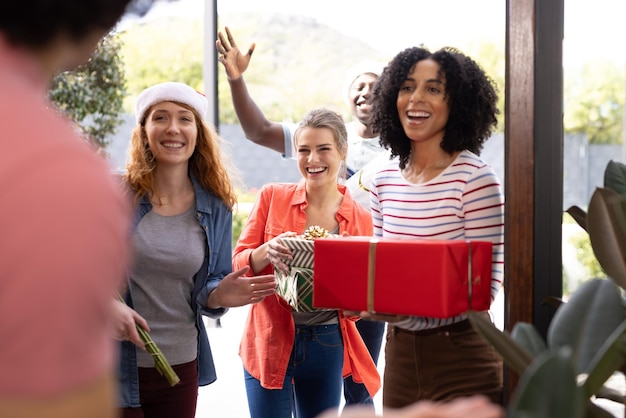 Foto felices amigos diversos saludando en la puerta con regalos en navidad