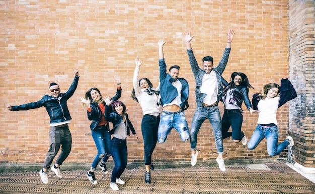 Foto felices amigos millennials saltando y animando contra la pared de ladrillos en la ciudad