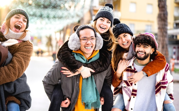 Felices amigos multiculturales caminando en el lugar de viaje de invierno en movimiento piggyback