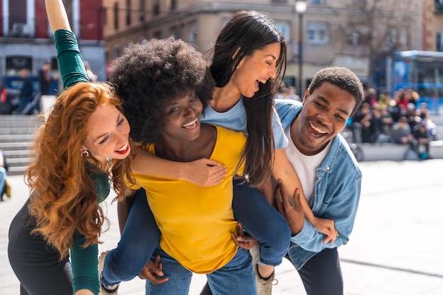 Felices amigos multiétnicos en la ciudad con subida en la espalda y sonriendo tomando un selfie