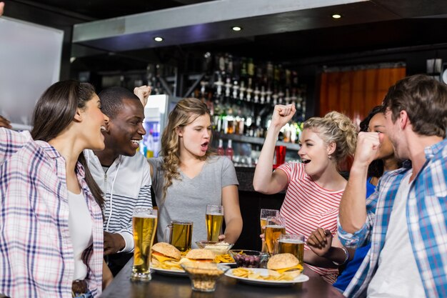 Felices amigos tomando una copa y viendo deporte