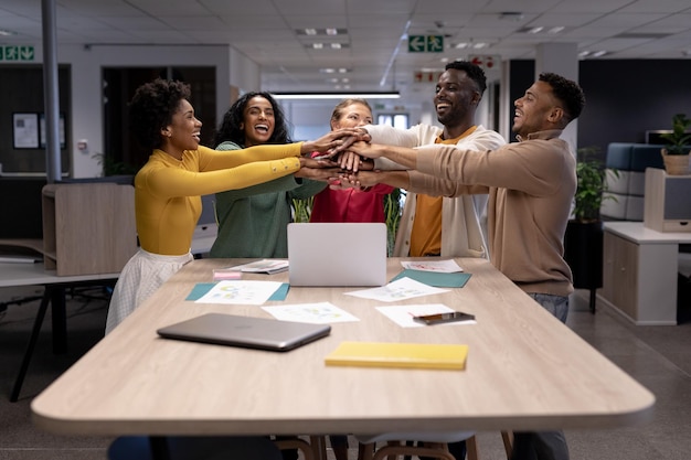 Felices asesores multirraciales apilando las manos sobre una computadora portátil durante una reunión en un lugar de trabajo moderno