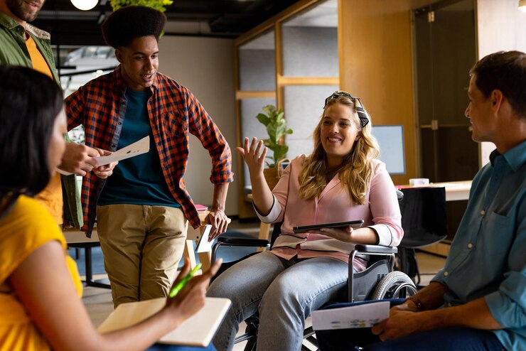 Foto felices colegas masculinos y femeninos diversos en discusión usando tableta en una reunión casual de oficina. oficina casual, trabajo en equipo, discapacidad, inclusión, negocios y trabajo, sin alteraciones.
