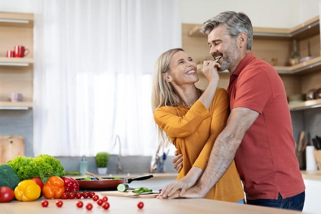 Felices cónyuges de mediana edad preparando una deliciosa cena juntos