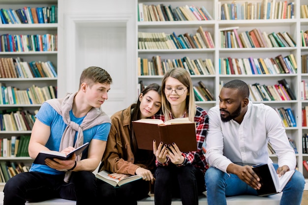 Felices cuatro jóvenes universitarios que estudian con libros en la biblioteca