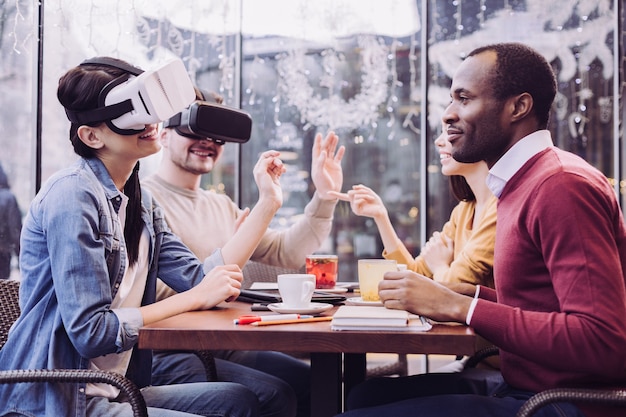 Felices dos amigos vigorosos que usan gafas de realidad virtual mientras sonríen y gesticulan