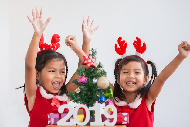 Felices dos muchachas asiáticas lindas del niño con números 2019 y el árbol de navidad