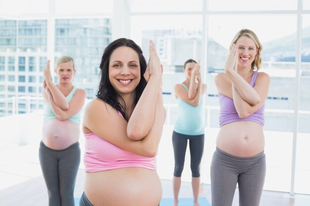 Felices embarazadas en clase de yoga de pie en pose de águila