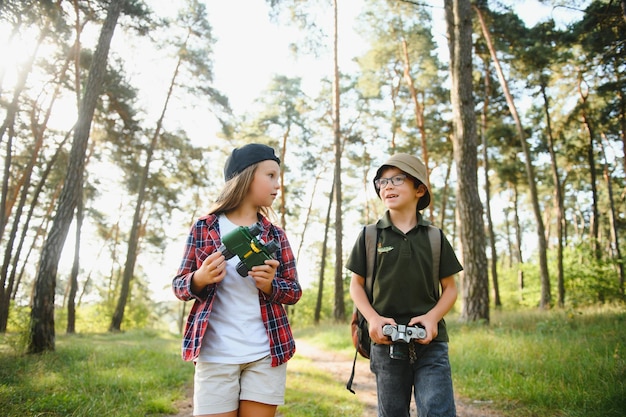 Felices y emocionados escolares con mochilas con ropa informal disfrutando de un paseo por el bosque en el soleado día de otoño dos niños activos niño y niña corriendo y jugando juntos durante un viaje de campamento en la naturaleza