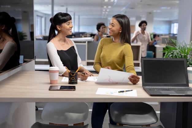 Felices empresarias multirraciales discutiendo sobre documentos mientras trabajan juntas en un lugar de trabajo moderno