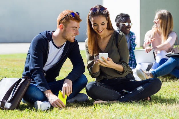 Felices estudiantes sentados afuera en el campus de la universidad.