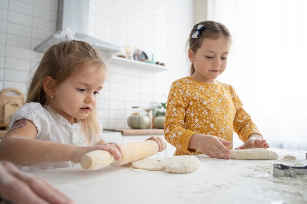 Felices hermanas niños niñas hornean galletas, amasan, juegan con harina y se ríen en la cocina.