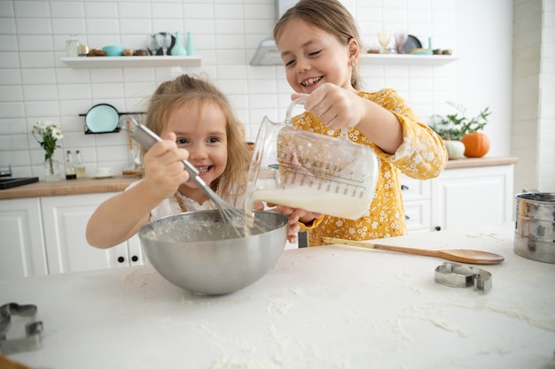 Felices hermanas niños niñas hornean galletas, amasan, juegan con harina y se ríen en la cocina.