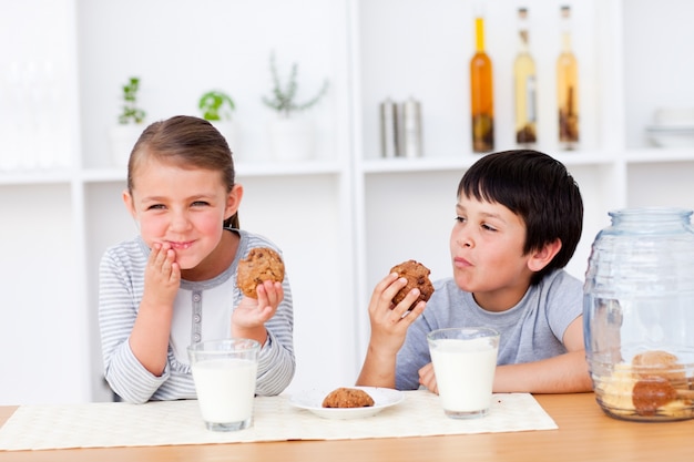 Felices hermanos comiendo galletas y bebiendo leche