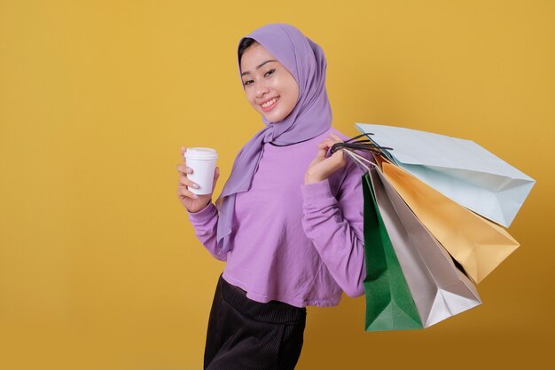 Felices hermosas mujeres asiáticas adictas a las compras traen un vaso de bebida y sostienen bolsas de compras, sonríen y alegres