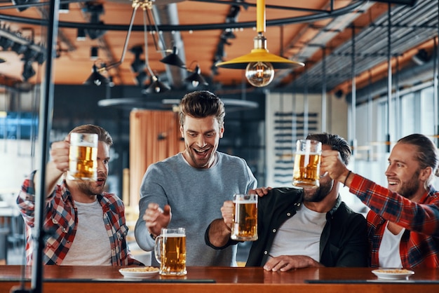 Felices los hombres jóvenes en ropa casual brindando con cerveza y sonriendo