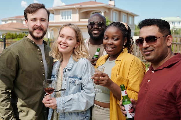 Felices jóvenes amigos interculturales con bebidas alcohólicas mirando a la cámara