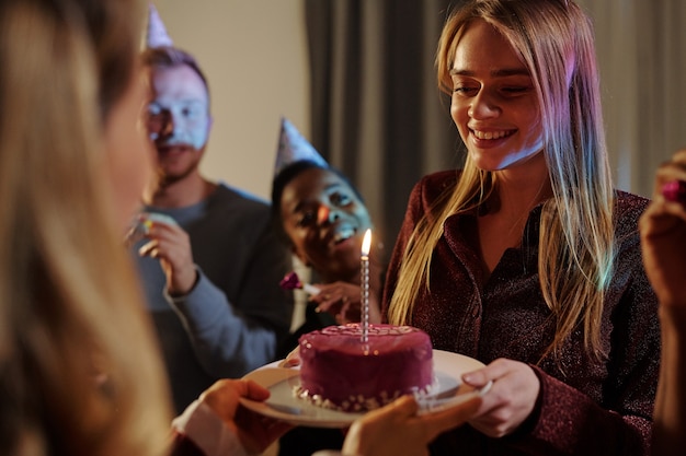 Felices jóvenes amigos interculturales felicitando a la niña sonriente en su cumpleaños mientras una de las mujeres pasa su plato con un delicioso pastel