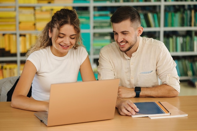 Felices jóvenes estudiantes de niño y niña preparándose en la biblioteca para el examen en la universidad Dos personas estudian Vista posterior de los libros