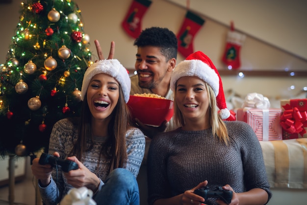 Felices juguetones amigos de navidad con sombreros de santa y suéteres disfrutando de casa para las vacaciones.